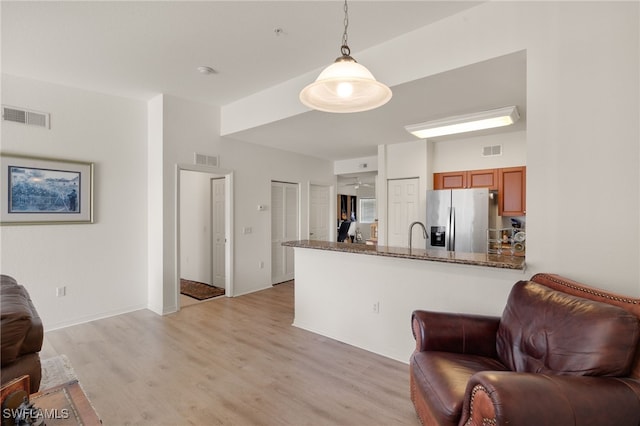 kitchen featuring kitchen peninsula, dark stone counters, decorative light fixtures, light hardwood / wood-style flooring, and stainless steel fridge with ice dispenser