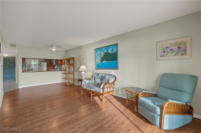 living area featuring hardwood / wood-style floors, ceiling fan, and a textured ceiling