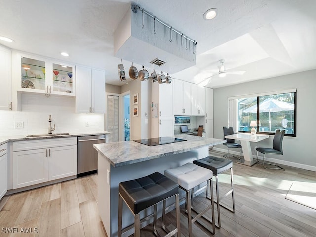 kitchen with black electric stovetop, stainless steel dishwasher, a breakfast bar, sink, and white cabinets