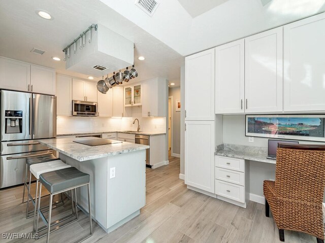 kitchen with sink, a kitchen island, light stone counters, white cabinetry, and stainless steel appliances