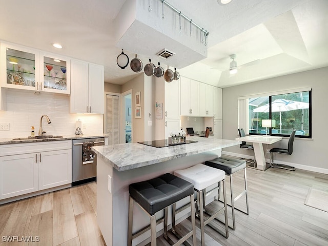 kitchen featuring a breakfast bar area, white cabinetry, a sink, stainless steel dishwasher, and black electric cooktop