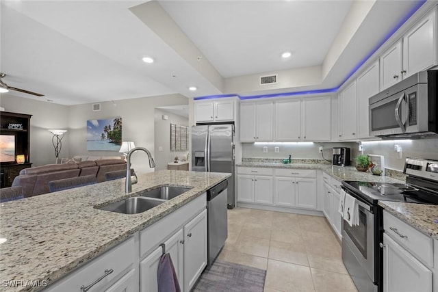 kitchen with light stone counters, stainless steel appliances, white cabinetry, and sink