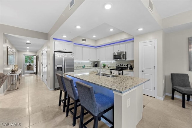 kitchen with appliances with stainless steel finishes, light stone counters, a breakfast bar, sink, and white cabinets