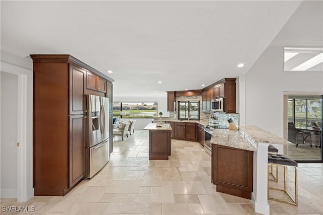 kitchen featuring light stone countertops, appliances with stainless steel finishes, tasteful backsplash, kitchen peninsula, and a breakfast bar area