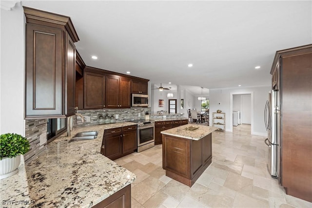 kitchen with light stone countertops, a center island, sink, hanging light fixtures, and stainless steel appliances