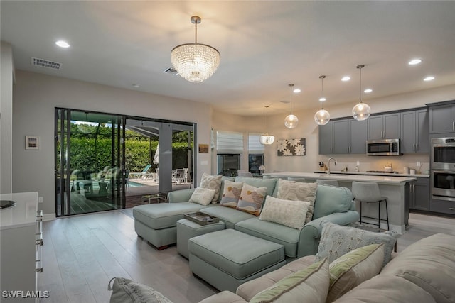 living room featuring sink, light hardwood / wood-style flooring, and an inviting chandelier