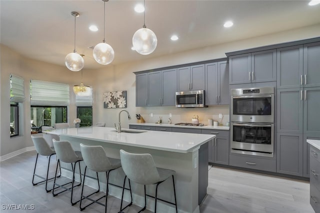 kitchen featuring pendant lighting, a kitchen island with sink, sink, and appliances with stainless steel finishes