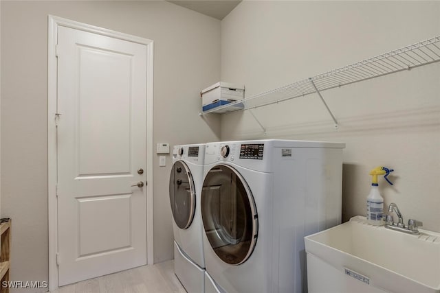 laundry area featuring sink, light hardwood / wood-style flooring, and washing machine and clothes dryer