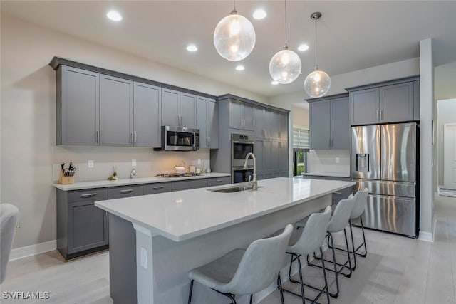 kitchen with decorative light fixtures, stainless steel appliances, a kitchen island with sink, and gray cabinetry