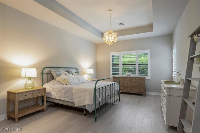 bedroom featuring a chandelier, light hardwood / wood-style flooring, and a tray ceiling