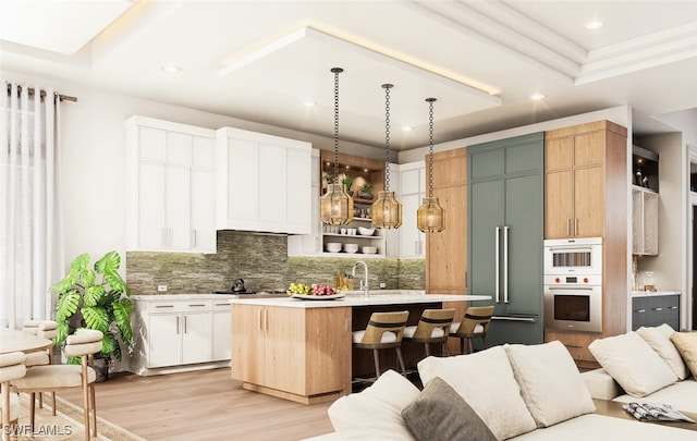 kitchen with decorative backsplash, a breakfast bar, double oven, white cabinetry, and an island with sink