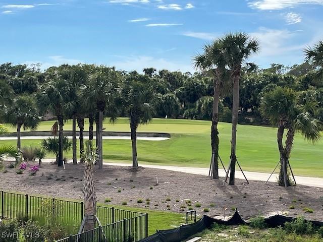 view of property's community featuring view of golf course, fence, and a lawn