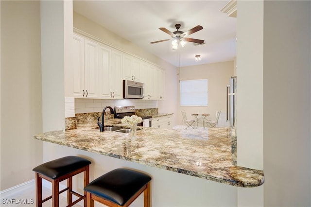 kitchen featuring white cabinetry, ceiling fan, light stone counters, backsplash, and appliances with stainless steel finishes