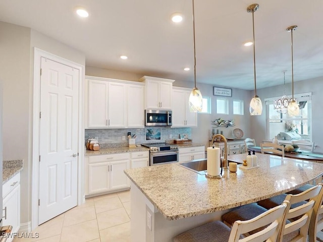 kitchen featuring a kitchen island with sink, stainless steel appliances, and decorative light fixtures