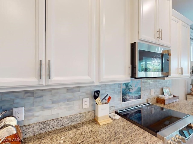 kitchen with white cabinets, stove, backsplash, and light stone countertops