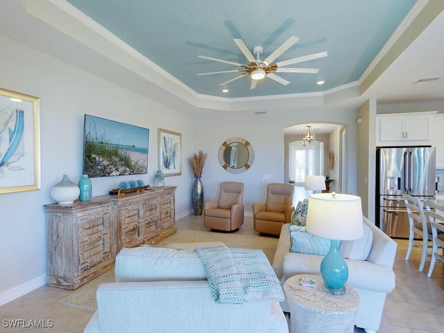 living room with ceiling fan with notable chandelier, light tile patterned floors, crown molding, and a tray ceiling