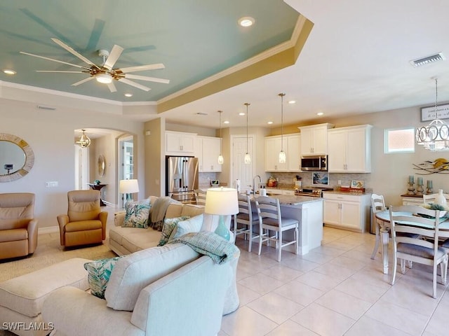 tiled living room featuring a tray ceiling, ceiling fan, sink, and ornamental molding