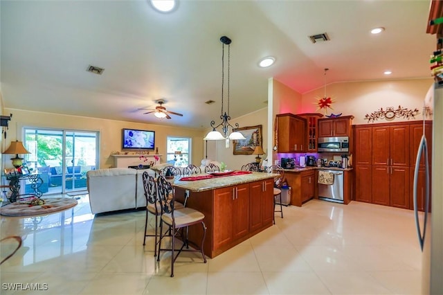 kitchen with pendant lighting, lofted ceiling, ceiling fan, a kitchen bar, and stainless steel appliances