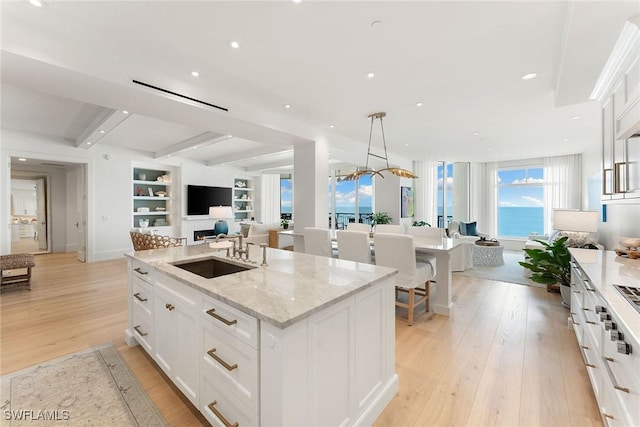 kitchen with beam ceiling, sink, white cabinets, and a center island with sink