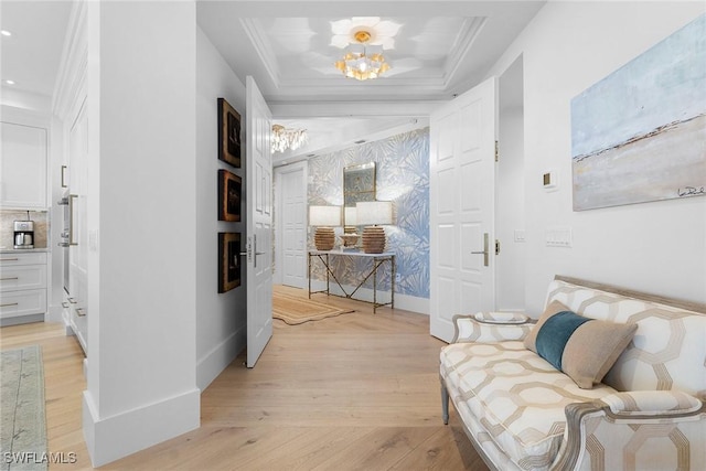 hallway with a tray ceiling, ornamental molding, a notable chandelier, and light wood-type flooring