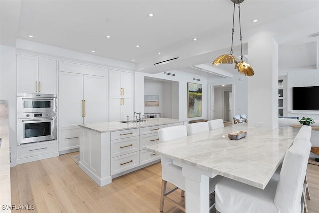 kitchen featuring a breakfast bar, white cabinets, hanging light fixtures, light stone counters, and a spacious island