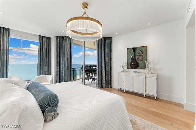 bedroom featuring access to exterior, light hardwood / wood-style flooring, a water view, and a wall of windows