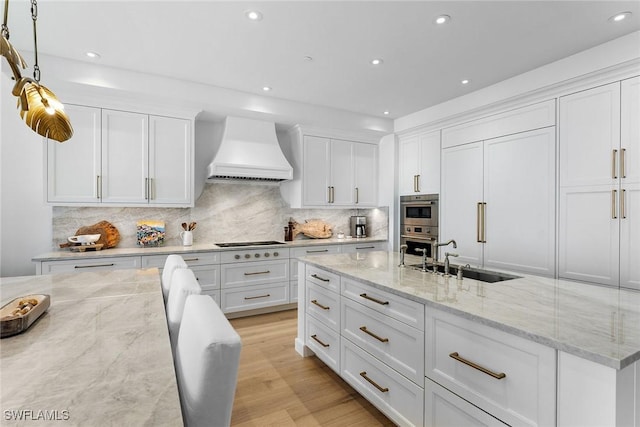 kitchen with white cabinetry, premium range hood, light stone countertops, and sink