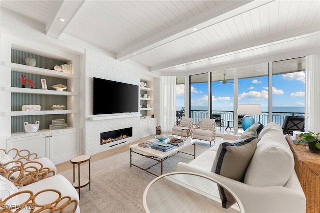 living room with a brick fireplace, built in features, beam ceiling, light hardwood / wood-style floors, and a wall of windows