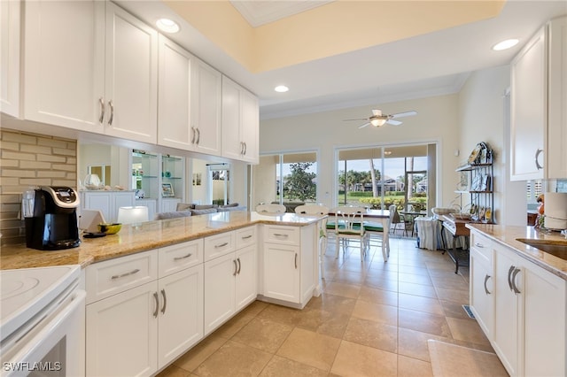 kitchen with white cabinets, ceiling fan, light stone countertops, ornamental molding, and kitchen peninsula