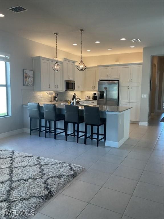 kitchen featuring stainless steel appliances, light tile patterned floors, pendant lighting, a breakfast bar area, and white cabinets