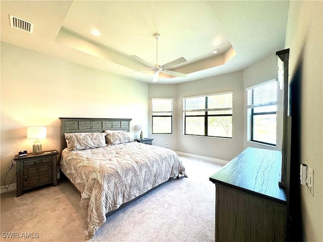 bedroom featuring light colored carpet, visible vents, a raised ceiling, and baseboards