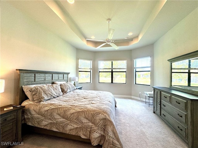 bedroom featuring baseboards, a raised ceiling, multiple windows, and light colored carpet