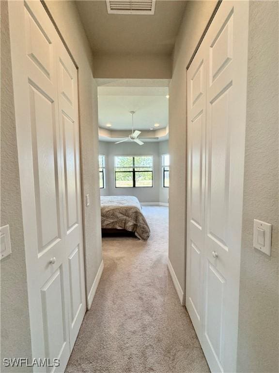 hall featuring baseboards, visible vents, carpet floors, and a textured wall