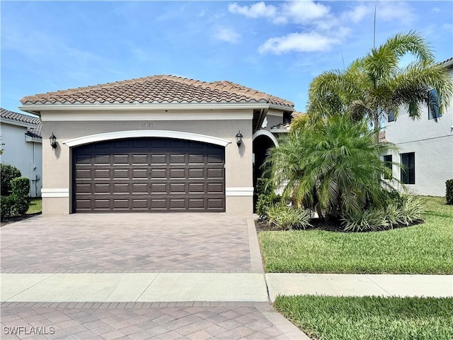 mediterranean / spanish house featuring stucco siding, decorative driveway, a tiled roof, and an attached garage