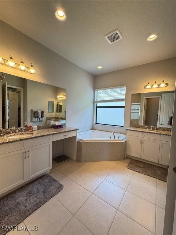 bathroom with visible vents, two vanities, a bath, and a sink