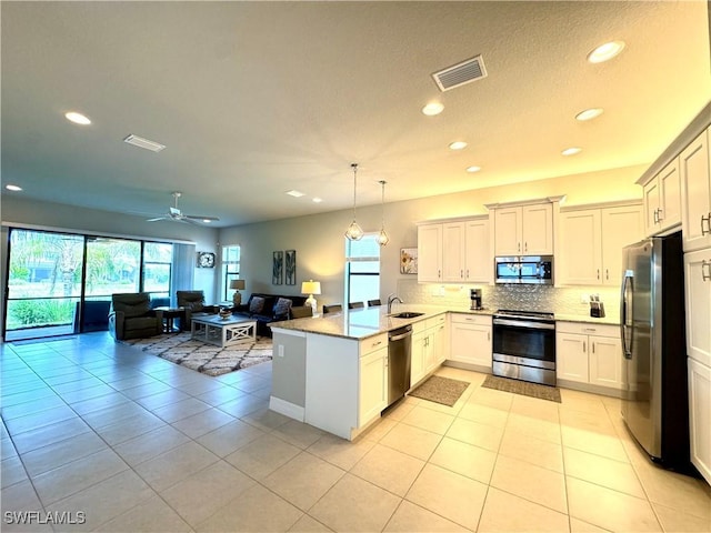 kitchen featuring a peninsula, stainless steel appliances, a sink, visible vents, and open floor plan