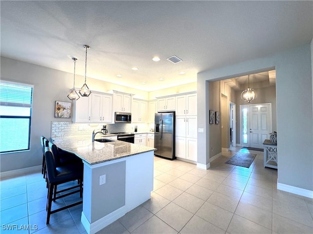 kitchen with light stone counters, stainless steel appliances, a sink, visible vents, and a peninsula