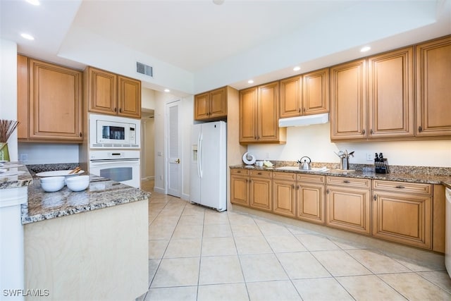 kitchen with sink, white appliances, light tile patterned floors, and dark stone counters