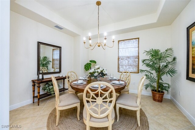 dining space with an inviting chandelier, light tile patterned flooring, and a tray ceiling