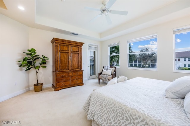 bedroom featuring ceiling fan, a tray ceiling, and light carpet