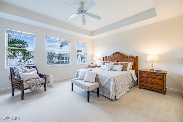 bedroom featuring ceiling fan, multiple windows, a raised ceiling, and light colored carpet