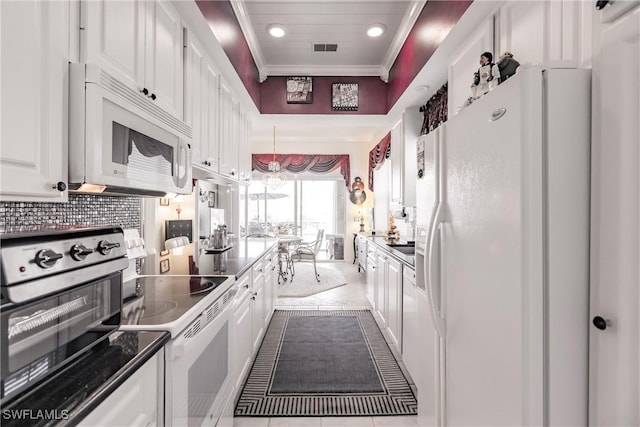 kitchen featuring white appliances, backsplash, tile patterned floors, hanging light fixtures, and white cabinetry