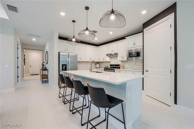 kitchen featuring decorative backsplash, appliances with stainless steel finishes, a kitchen island with sink, sink, and white cabinets