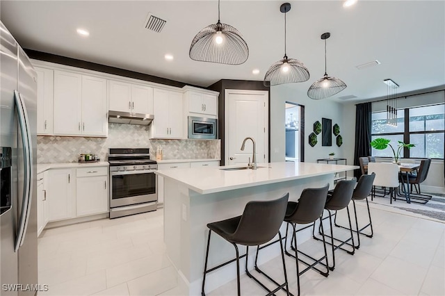 kitchen featuring white cabinetry, sink, stainless steel appliances, decorative light fixtures, and a center island with sink