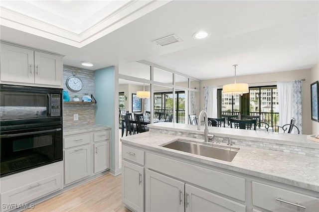 kitchen featuring pendant lighting, black appliances, sink, light wood-type flooring, and light stone countertops