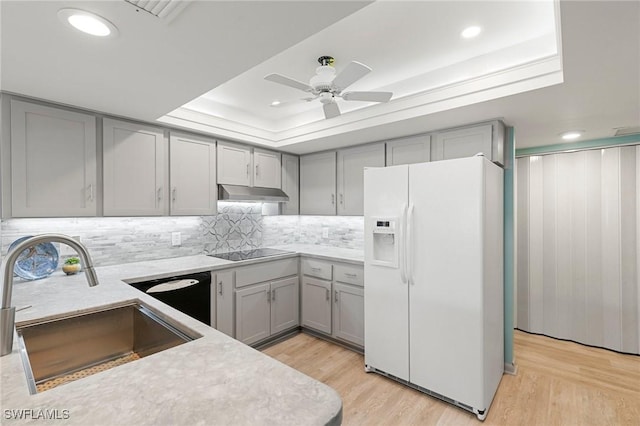 kitchen featuring a raised ceiling, dishwasher, white refrigerator with ice dispenser, and light wood-type flooring