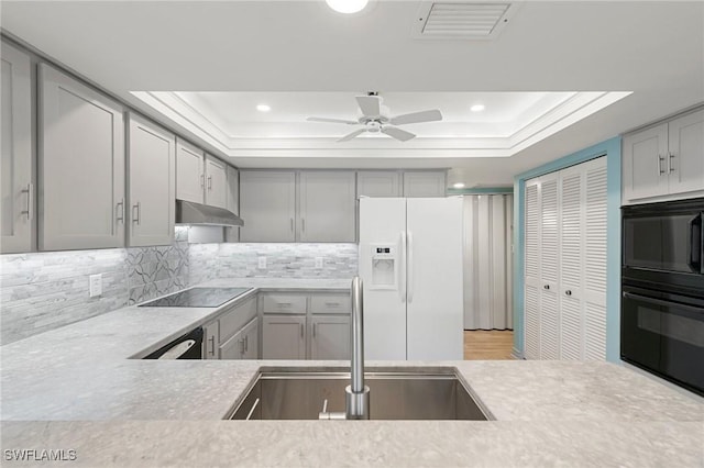 kitchen featuring black electric stovetop, sink, gray cabinets, white fridge with ice dispenser, and a tray ceiling