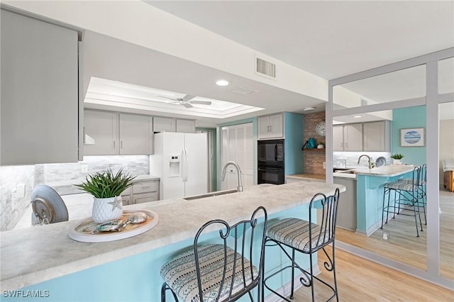 kitchen featuring a kitchen bar, tasteful backsplash, gray cabinetry, sink, and black appliances