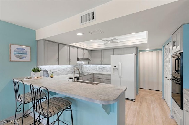 kitchen with white fridge with ice dispenser, sink, a raised ceiling, kitchen peninsula, and black oven