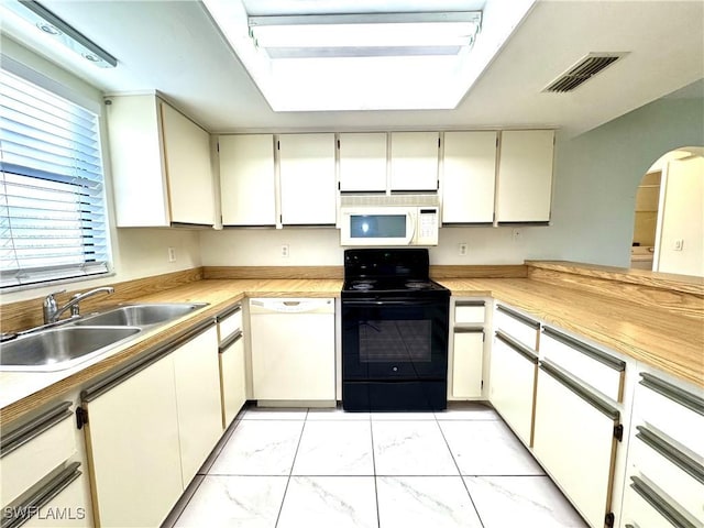 kitchen with white cabinets, white appliances, sink, and a skylight